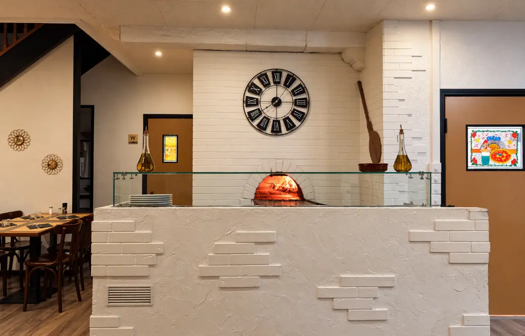 Comptoir blanc en briques avec le four à bois allumé, surmonté d'une grande horloge murale
